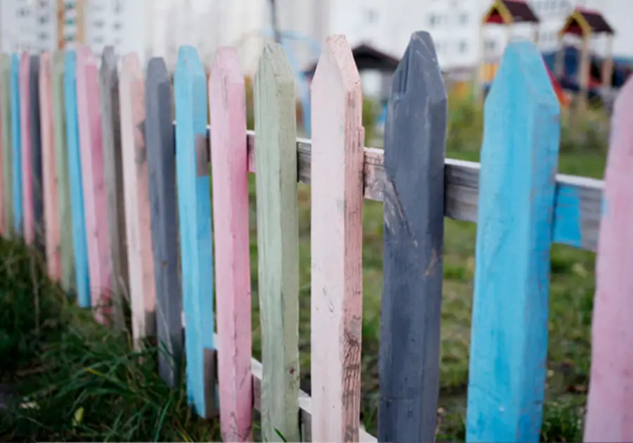 A wooden fence painted in calming shades of charcoal grey, blue, pink and green. The colourful design adds a cheerful and welcoming touch to the surroundings, making it an appropriate choice for creating a visually appealing boundary.